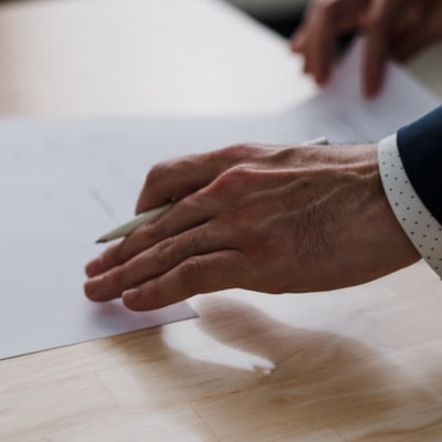 estate-planning-30 A hand holding a pen touching a document on a desk. It seems like the person holding the pen is about to sign the document.